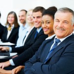 Cheerful senior business man in an office environment with his colleagues in the background